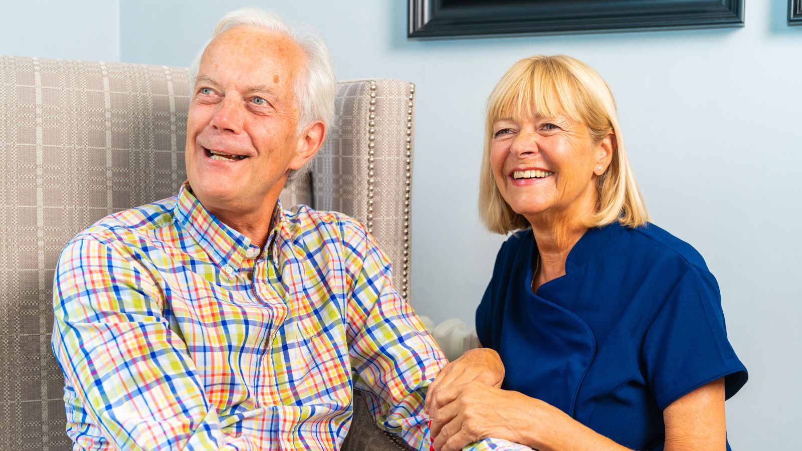 A resident sat in a comfortable armchair talking to a member of staff