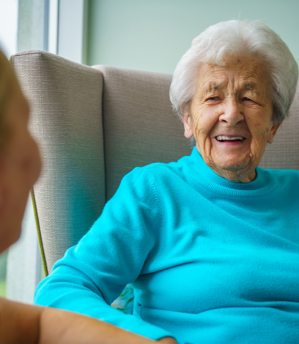 Elderly resident sits smiling at care worker